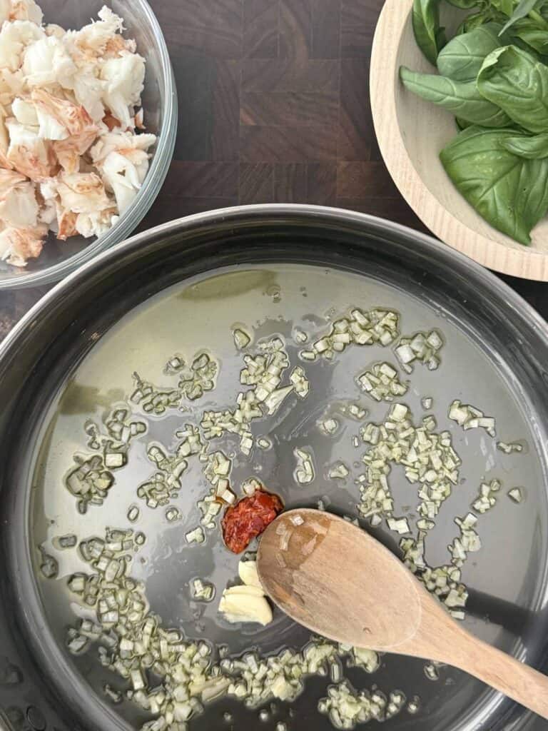 A large skillet is sauteeing garlic chilies, and shallot with a wooden spoon.