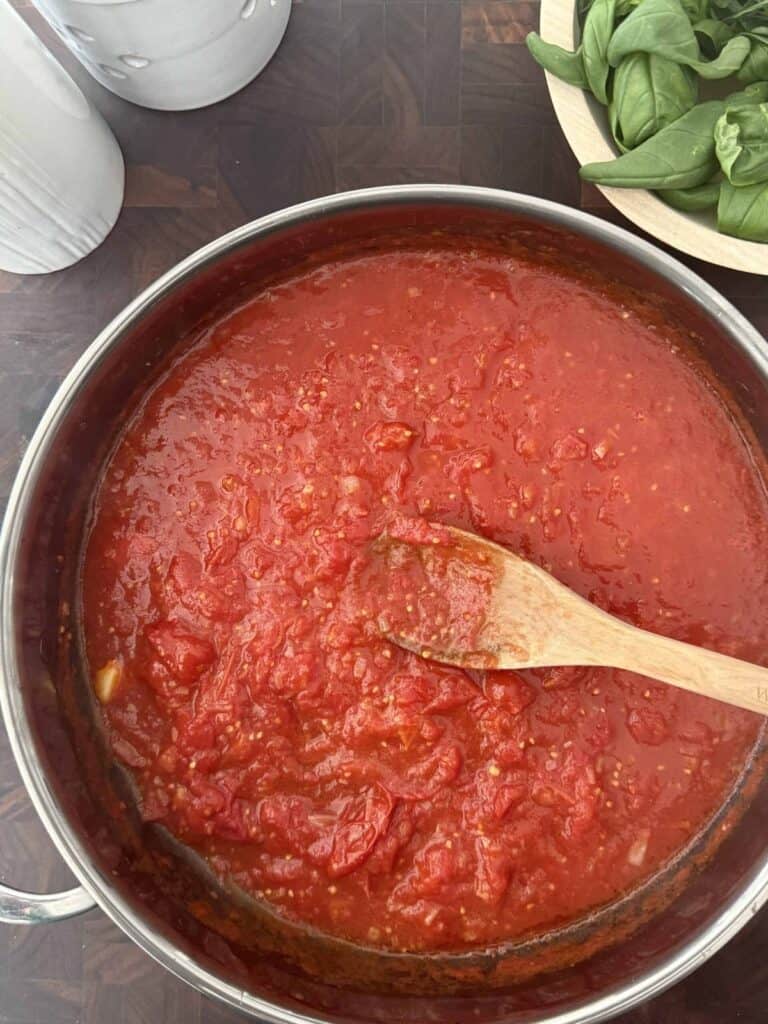 Crushed tomatoes are added to the large skillet with a wooden spoon.