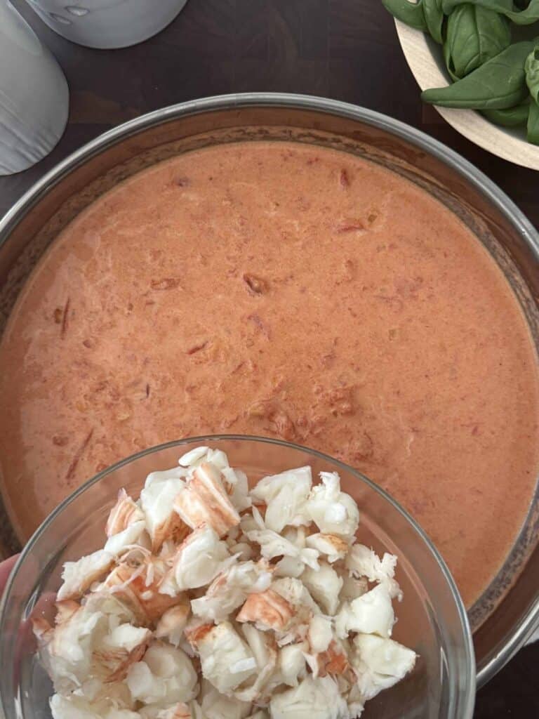 Chopped cooked lobster meat is in a glass bowl and being added to the creamy tomato sauce in the large skillet.