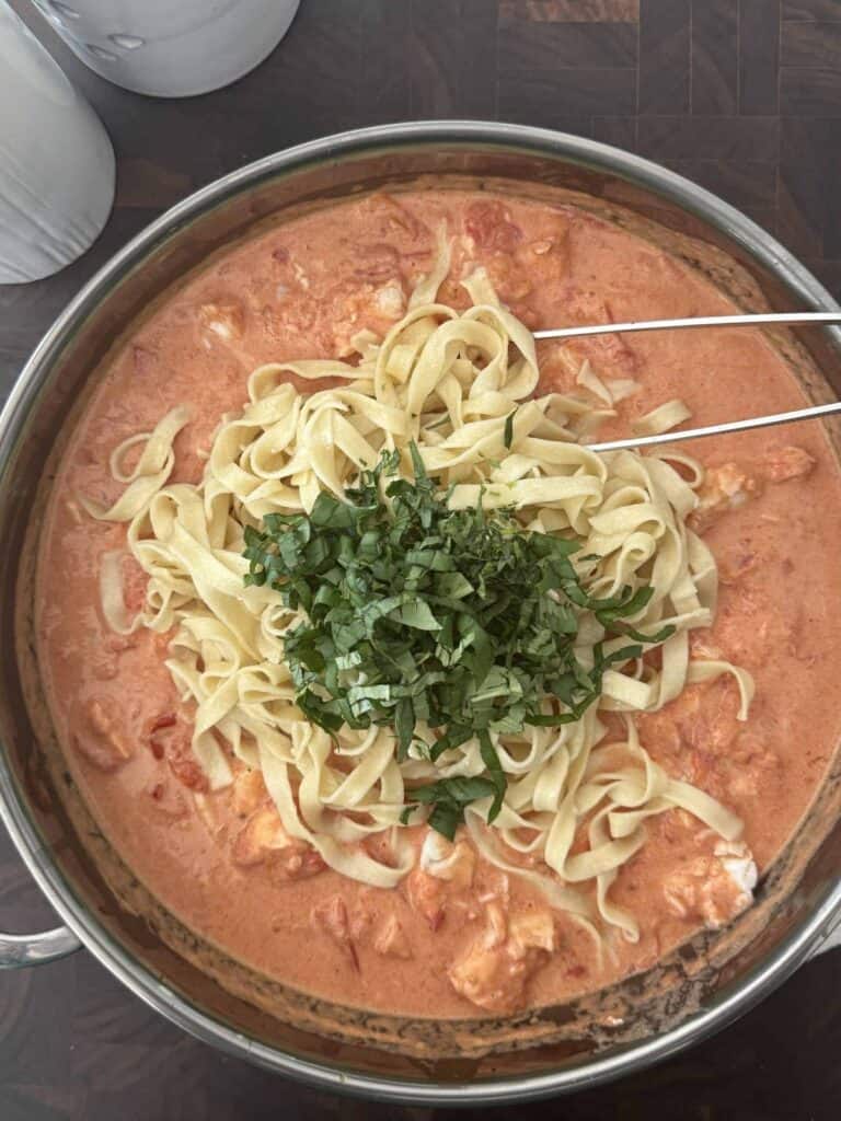 Cooked pasta, basil, and tarragon are stirred into the creamy tomato sauce in the large skillet.