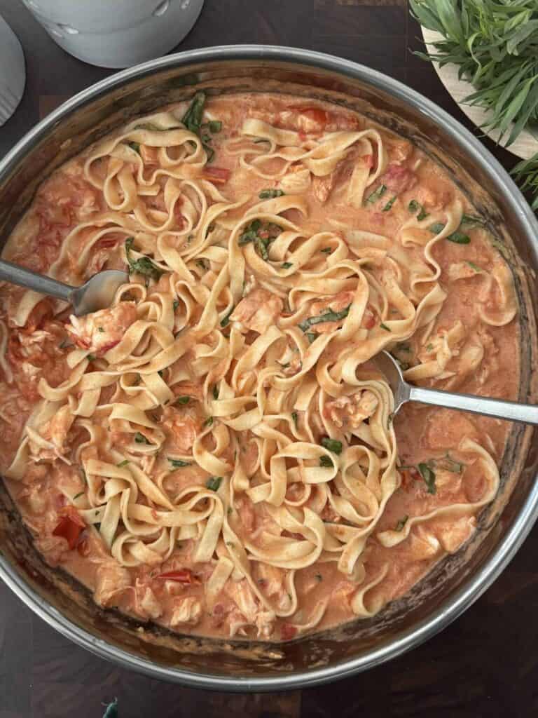 Finished creamy lobster pasta in a large skillet with two large metal serving utensils.