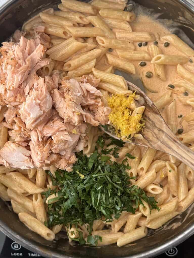 A large skillet with the final ingredients added to finsh the smoked salmon pasta. Fresh chopped basil & parsley, lemon zest, and the smoked salmon pieces ready to be folded into the pasta and cream sauce.