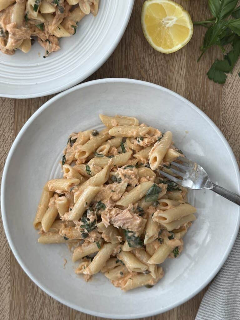 Smoked salmon pasta served in white pasta bowls with a fork, and lemon slices and fresh parsley in background.