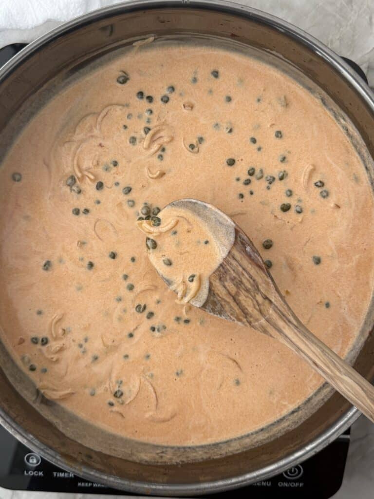 A large skillet with the ingredients for the smoked salmon pasta just after heavy whipping cream has been added tomake a pink sauce.