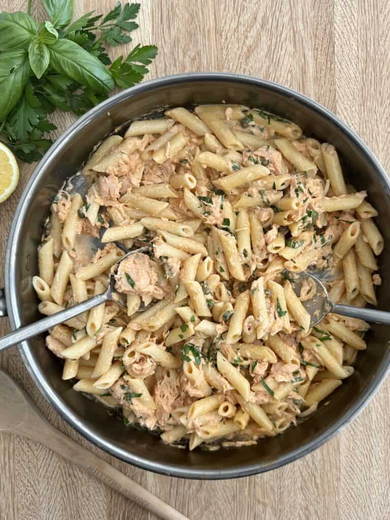 A photo of the finished smoked salmon pasta in a skillet with two large serving spoons.