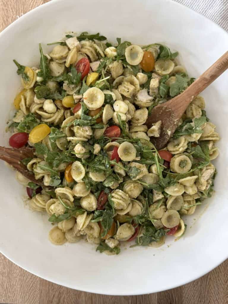 Orzo pasta salad in a large white bowl with two wooden spoons.