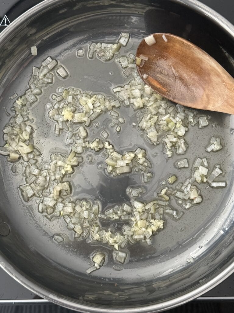 overhead shot f onnion and garlic sauteeing in a skillet with a wooden spoon.