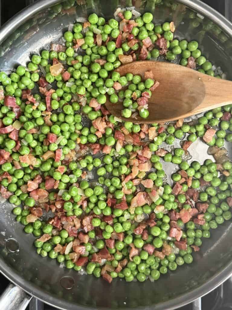 Sautéed pancetta and peas in a skillet, stirred with a wooden spoon as the base for pasta e piselli.