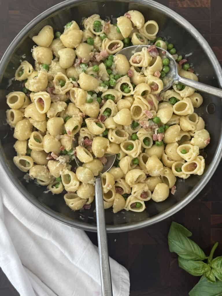 Finished pasta e piselli in a stainless steel skillet, with orecchiette, peas, pancetta, and cheese stirred together, ready to serve.